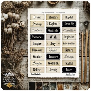 May include: A collection of rectangular labels with inspirational words like "Dream," "Adventure," and "Peace." The labels are in various colors, including black and cream, with elegant fonts. The image includes pencils, dried flowers, and the text "Soul Labels."