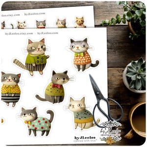 Op de afbeelding: Een vel met ge&iuml;llustreerde kattenstickers, elk met unieke outfits en poses. De katten zijn afgebeeld in verschillende kleuren, waaronder groen, geel en oranje. De stickers staan op een wit vel met de tekst "by JLeeLoo" en "created with love".