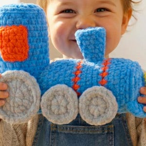 May include: A handmade blue crochet train toy with orange and grey accents. The toy features a rectangular orange shape on the front, grey wheels, and orange stitching details. A fun and colourful toy for children.