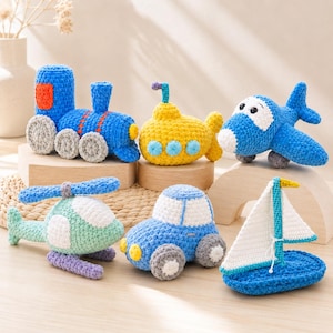 Può includere: Una collezione di sei giocattoli all'uncinetto composta da un treno blu con ruote grigie, un sottomarino giallo, un aeroplano blu, un elicottero verde menta, un'auto blu con finestrini bianchi e una barca a vela blu e bianca con albero turchese.