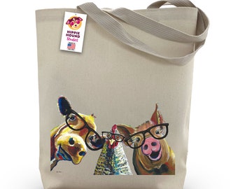 May include: A beige canvas tote bag featuring a colorful illustration of a cow, chicken, and pig wearing glasses. The bag has a tag that reads "Hippie Hound Studios" and "Made in the USA". The tote bag has two beige handles.