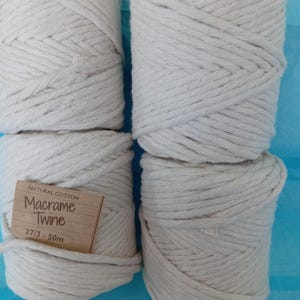 May include: Four spools of natural cotton macrame twine, tightly wound and off-white in colour. A small brown tag is visible on one spool, with the text "Natural Cotton Macrame Twine 27/3 - 50m". The twine is suitable for various craft projects.