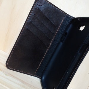 May include: A dark brown leather wallet-style phone case featuring a black interior plastic shell. The leather cover includes three vertical card slots and is stitched with light brown thread along the edges, providing a secure fit for a mobile device.