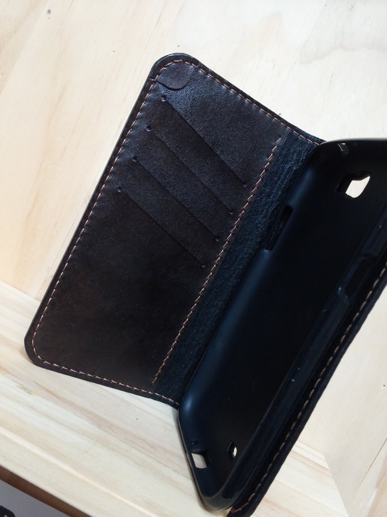 May include: A dark brown leather wallet-style phone case featuring a black interior plastic shell. The leather cover includes three vertical card slots and is stitched with light brown thread along the edges, providing a secure fit for a mobile device.
