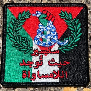 May include: Square patch with a black border, featuring a design with the colors of the Palestinian flag: green, red, white, and black. The patch includes a coiled snake, a green hand, and Arabic text.