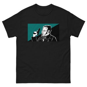 May include: Black t-shirt featuring a graphic of a man in a suit holding a gun. The graphic is in black and white with teal and black background. The man is wearing glasses and a bow tie.