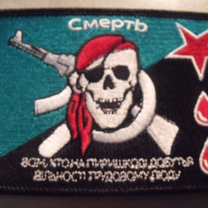 May include: A black and teal embroidered patch with a skull and crossbones, a red star, and the Russian word "Смерть" (Death). The patch also features a red bandana, a rifle, and three red blood drops. The text at the bottom reads "Всм кто на пирацкой догма влилось, трудящему люду".