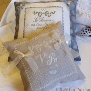 Peut inclure: Deux coussins carrés décoratifs avec broderies. L'un porte l'inscription "L'Amour un lien d'union parfa", l'autre les initiales "TR" et la date "25.07.15". Les deux coussins sont ornés de nœuds en ruban.
