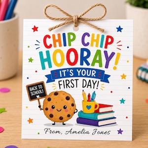 Op de afbeelding: Een vierkante witte kaart met lijntjespapier-textuur, voorzien van de tekst CHIP CHIP HOORAY! IT'S YOUR FIRST DAY! en From, Amelia Jones. Een cartoon koekje met chocoladestukjes houdt een bordje BACK TO SCHOOL! vast bij boeken en potloden.