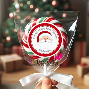 May include: A large, round Christmas lollipop in a clear cellophane bag, tied with a white ribbon. The lollipop has red, white, and green stripes and a circular sticker with Santa Claus and the text "Wishing you a Very Merry Christmas".