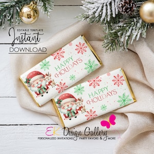 Może przedstawiać: Dwa opakowania czekolady o świątecznym designie. Każde opakowanie zawiera ilustrację Świętego Mikołaja, renifery, płatki śniegu i napis "HAPPY HOLIDAYS" w kolorze czerwonym i zielonym. Opakowania mają złote krawędzie i są umieszczone na białym tle.