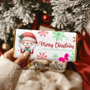 Peut inclure: Emballage de barre chocolatée de Noël avec le Père Noël, des flocons de neige et l'inscription "Merry Christmas". Le bord est doré et un papillon rose est présent. Le texte "Wishing You a Wonderful Holiday Season" est également inclus.
