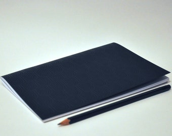 May include: A black notebook with a subtle patterned cover and a black pencil lying on top of it.