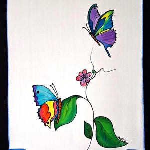 May include: A white textile featuring two colorful butterflies and a flowering vine. One butterfly has blue, purple, and yellow wings, while the other has blue, orange, and yellow wings. The vine has green leaves and a pink flower.