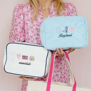 May include: A light blue pouch with a cowboy boot, smiley face, and the text Ragland, a white pouch with navy trim featuring a bow, American flag, dog, and the text essentials, and a white canvas tote with pink trim, the text PBC, and patches.