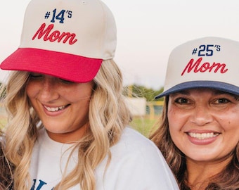 Può includere: Tre cappellini da baseball con corona color bianco sporco e visiere colorate. Il cappellino a sinistra ha una visiera blu navy e la scritta #35's Mom in rosso. Il cappellino centrale ha una visiera rossa e la scritta #14's Mom in rosso.