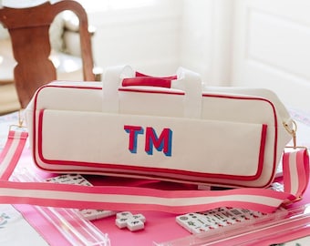 May include: A white rectangular canvas bag with red piping and a detachable pink and white striped shoulder strap. The front features the letters TM in blue and red. The bag is accompanied by clear acrylic racks and white mahjong tiles.