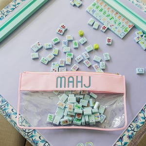 A pink and green table with a clear plastic bag filled with colorful tiles, and a set of dominoes on the table.