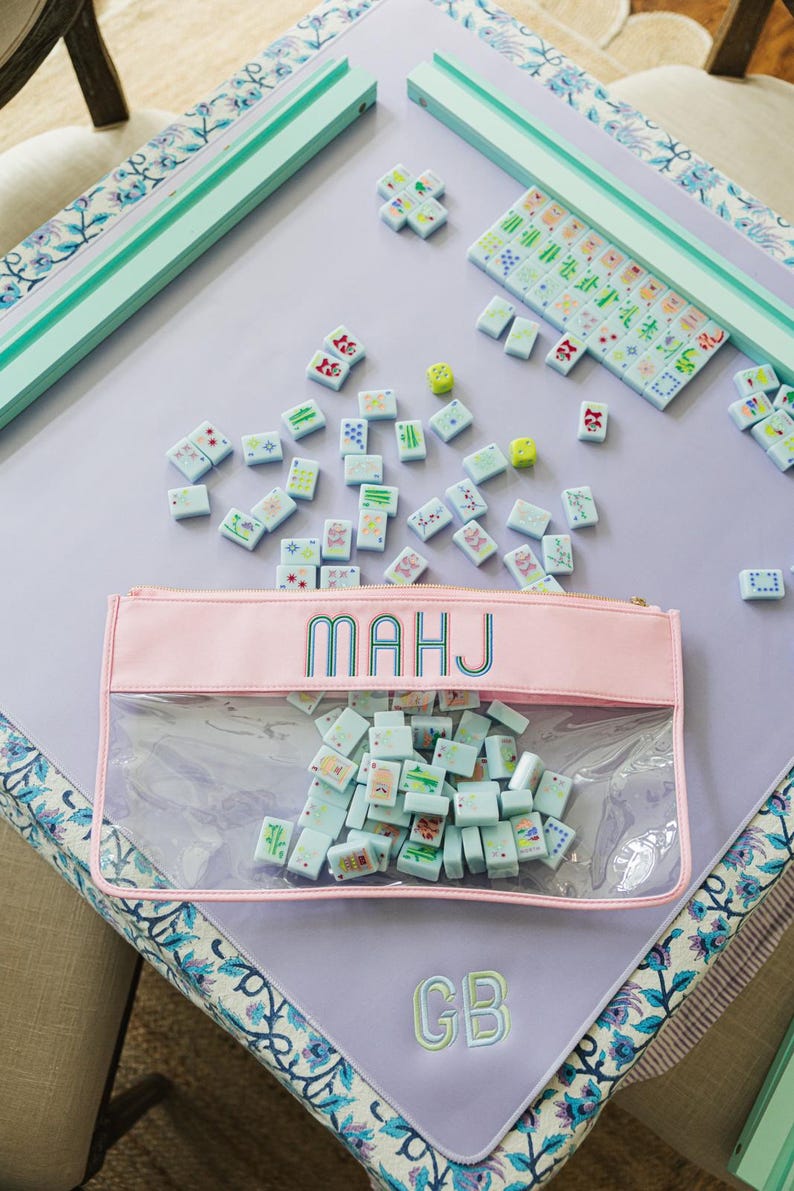 A pink and green table with a clear plastic bag filled with colorful tiles, and a set of dominoes on the table.