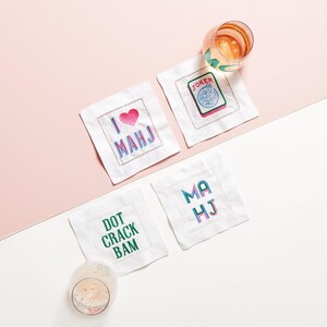 a set of three cocktail napkins with various phrases and designs, along with a glass of wine and a glass of beer on a pink background.
