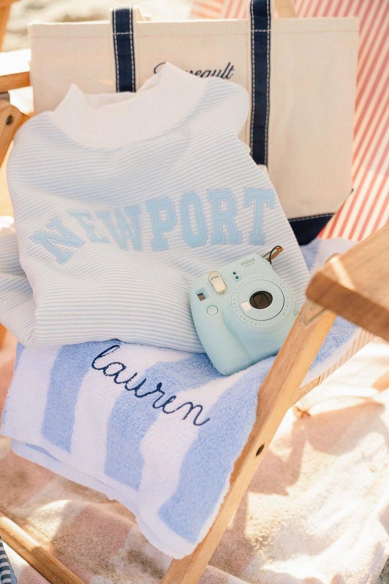 A white and blue striped towel with the name "Laurel" printed on it, along with a small blue camera, is placed on a wooden chair.