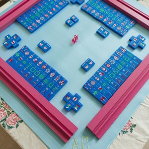 A colorful game board with blue tiles and pink pieces, arranged on a table with a floral tablecloth.