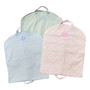 May include: Three garment bags with floral patterns and embroidered initials. One bag is light blue with blue trim and initials, another is light green with initials, and the third is pink with initials.