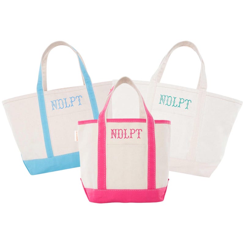 May include: Three canvas tote bags in white with colored accents. One has light blue trim and handles, another has pink trim and handles, and the third has light green accents. Each bag has the embroidered letters "NDLPT".
