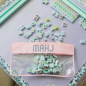 A pink and green table with a clear plastic bag filled with colorful tiles, and a set of dominoes on the table.