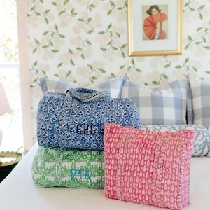 a bedroom with a bed, a framed picture on the wall, and three colorful bags or pillows on the bed.