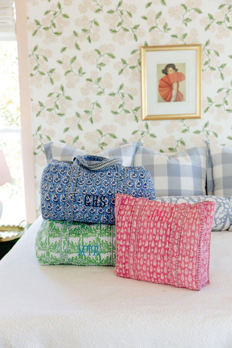 a bedroom with a bed, a framed picture on the wall, and three colorful bags or pillows on the bed.