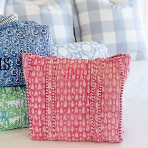a bed with a pink patterned pillow, a blue and white checkered pillow, and a green and white patterned pillow.