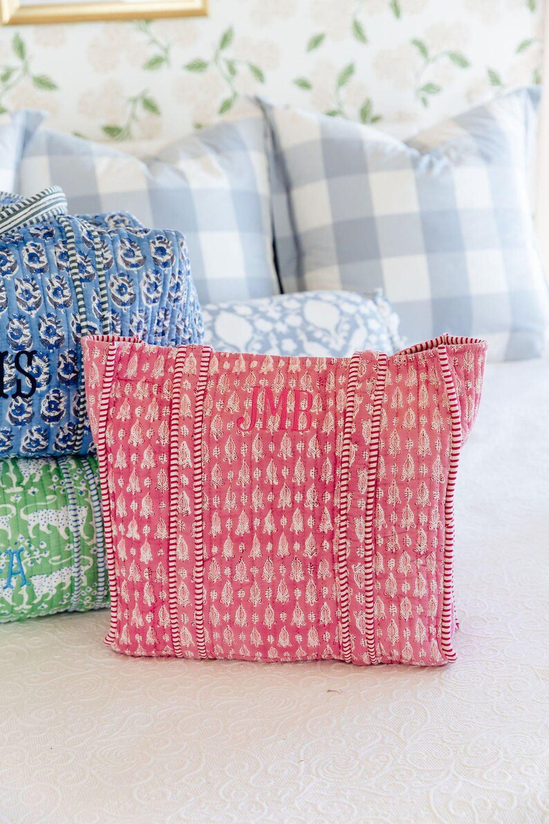 a bed with a pink patterned pillow, a blue and white checkered pillow, and a green and white patterned pillow.