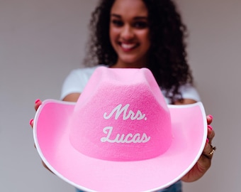 May include: A pink cowboy hat with a white brim and the text "Mrs. Lucas" embroidered on the front.