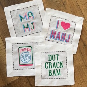 four square cocktail napkins with various embroidered text and designs.