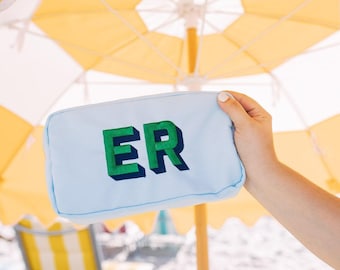 May include: A light blue rectangular zippered pouch featuring the letters ER embroidered in a bold green font with a dark green shadow effect. The pouch is constructed from a smooth fabric material and has a simple, functional design.