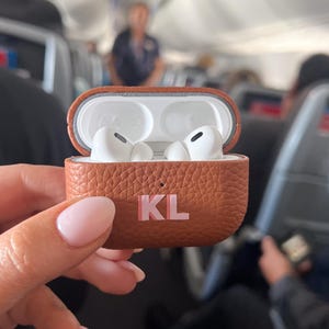a person holding a case with two airpods in it
