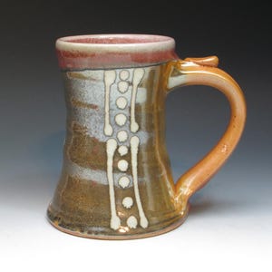 May include: A brown ceramic mug with a white and brown design. The mug has a rounded body and a handle. The mug is glazed with a brown and white glaze.