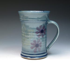 May include: A blue ceramic mug with a light blue glaze and two purple flowers painted on the side.