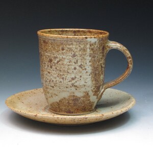May include: A speckled brown and cream ceramic coffee mug with a handle, sitting on a matching saucer.