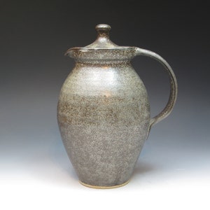 May include: A ceramic pitcher with a lid, featuring a speckled gray glaze. The pitcher has a rounded body and a handle.