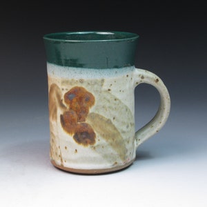 May include: A ceramic mug with a green glaze on the top and brown and white glaze on the bottom. The mug has a handle and is a light brown color.