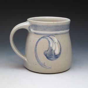 May include: A ceramic mug with a light grey glaze and a blue and white design. The mug has a rounded body and a handle.