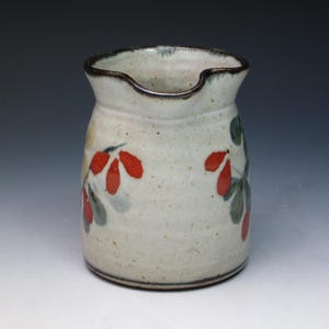 May include: A white ceramic pitcher with a brown rim and red and green floral designs.