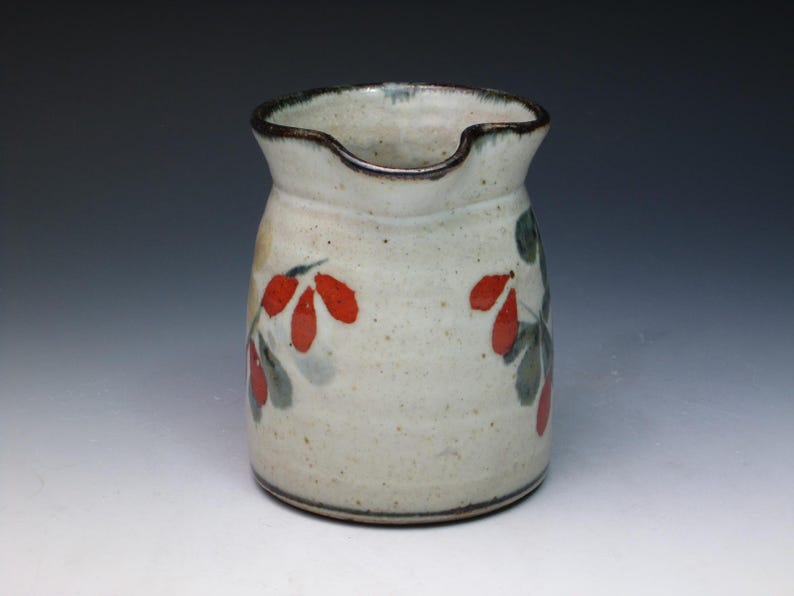 May include: A white ceramic pitcher with a brown rim and red and green floral designs.