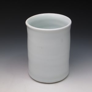 May include: A white ceramic cup with a smooth, rounded shape. The cup is empty and has a slightly off-white color.