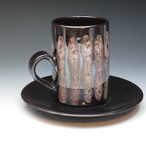 May include: A black and brown ceramic coffee mug with a unique striped pattern. The mug is sitting on a matching saucer.