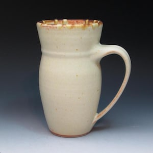 May include: A white ceramic mug with a brown rim and handle. The mug has a slightly rounded shape and a speckled glaze.