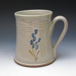 May include: A beige ceramic mug with a brown handle and a blue flower design.