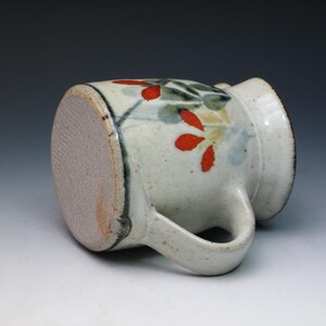 May include: A white ceramic mug with a handle, decorated with a floral design in red, green, and blue.